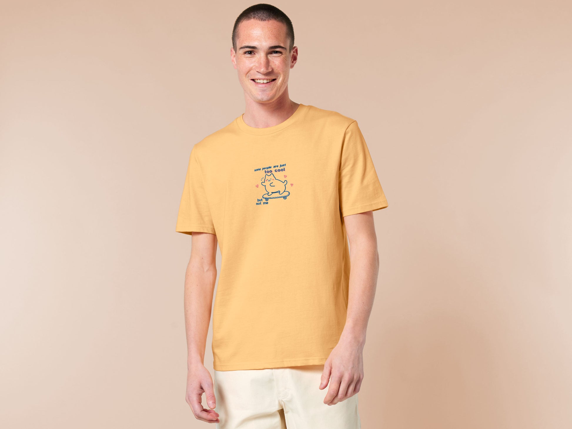 Light yellow short sleeve t-shirt with embroidered pink and blue design of a cute chibi skateboarding cat with the text some people are just too cool but not me.
